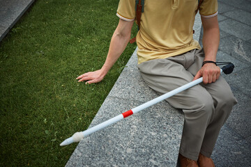 Blind man resting on stone edge touching grass with hand. Concept of sensory experience,...
