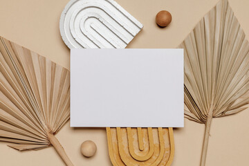 Blank paper mockup card on ceramic stands with dry palm leaves on light brown background. Paper postcard for blog, invitation, greeting, logo, wedding or design