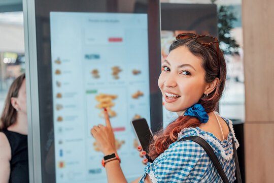 Customer girl ordering food at a fast food restaurant, interacting with a self service electronic menu on a touchscreen kiosk for a quick meal choice