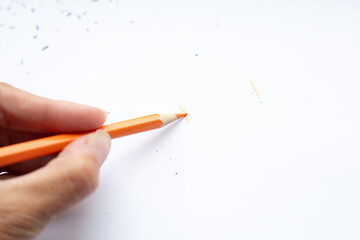 A person holds an orange pencil in hand on a piece of paper