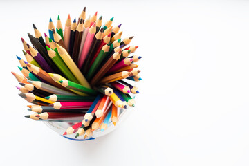 A glass container full of colorful pencils on a white background