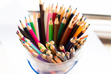 A bucket that is filled with various colored pencils resting on a table