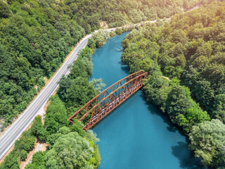 Aerial view of an old rusty metal bridge crossing a blue river near an asphalt road surrounded by...