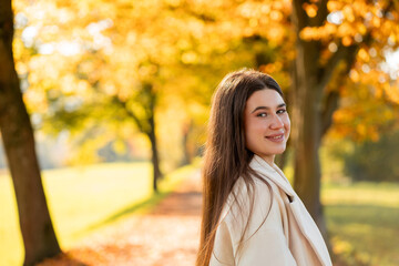 Season. Portrait of a young woman in a cozy coat in an autumn park. Yellow leaves of trees.