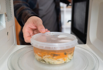 Hand placing soup container into microwave for heating.	
