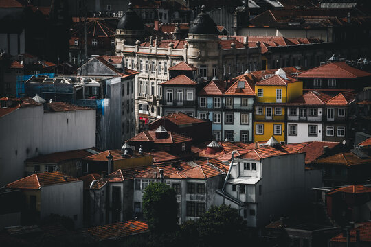 Porto, Portugal - 17 June 2022: View of terracotta roofs cascading down the hillside, punctuated by vibrant yellow and blue facades against a backdrop of domed buildings.
