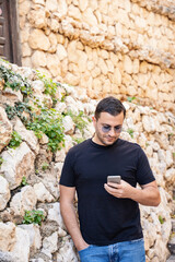 Adult man in sunglasses standing with smartphone in old town of Guadalest in Spain