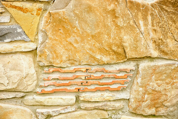 Close-up of a textured stone wall with warm earthy tones and unique red brick inlay, perfect for architectural or background use.