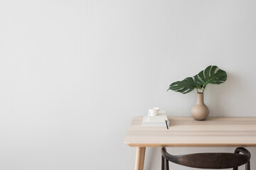 Minimal Scandi interior. Wooden table, vase, white book and coffee cup. Soft natural light, calm cozy atmosphere. Home office. Empty gray wall background