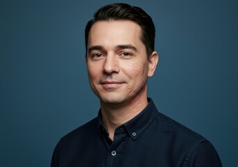 Man smiling confidently in blue shirt against dark background  