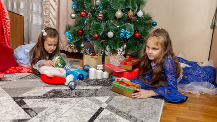 Little children enjoying Christmas, sisters lying on the floor and looking at boxes. Happy...