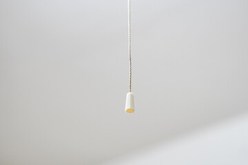 A single, simple, off-white light cord fixture hangs from a white ceiling.