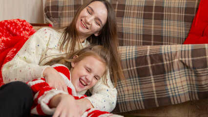 Happy family having fun at home for Christmas. Mother tickles her daughter sitting on the floor. Festive cozy interior