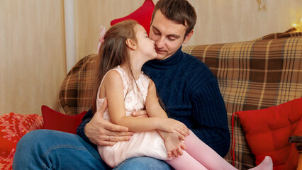 Father and beautiful little daughter sitting on sofa with christmas decoration