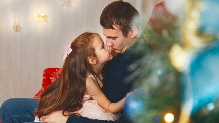 Portrait of a loving daughter kissing her father near the Christmas tree and celebrating Christmas at home.