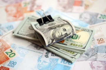 Bunch of US dollar bills lies on big amount of Brazilian reais banknotes close up