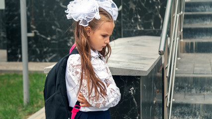 Schoolgirl sadness standing against modern school. Long-haired girl feels bullied by classmates at school