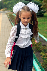 Portrait of school girl with backpack smiling posing on camera near campus. Female elementary school student standing on stairs outside school building.