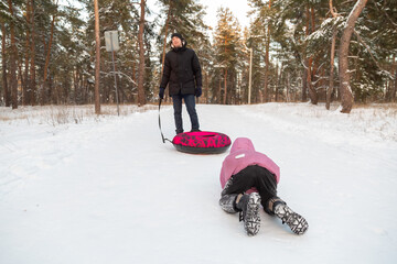 Father and daughter having fun with snow tube in the forest