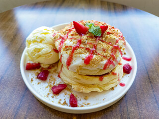 plate of fluffy Japanese souffle pancakes topped with whipped cream, crushed graham crackers, strawberry sauce, fresh strawberry slices, and a scoop of vanilla ice cream on the side.