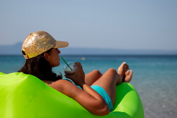 Portrait of a cute woman drinking cold chocolate and lying on the green inflatable sofa on a summer...