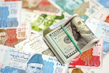 Stack of US dollar bills lies on big amount of Pakistan rupees banknotes close up