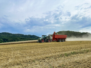 Obraz premium A combine harvester unloads its hopper into a tractor trailer. Harvesting wheat from the fields. Herbicides and pesticides for high yields. High quality photo