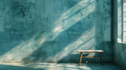 Empty room with teal textured stucco wall and wooden bench illuminated by natural sunlight from a window, abstract background.