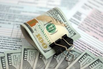 Big amount of United States dollar bills on table with 1040 tax return form