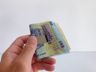 Romanian lei bank notes held in hand in a money clip against a white background