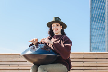young caucasian woman playing black handpan with hands, ethnic metal drum instrument, sits on...