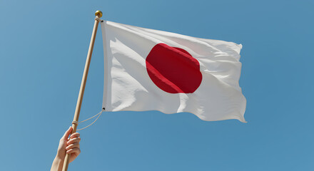 Japanese flag, white with red sun disk, held against a clear blue sky, symbolizing national pride and identity.