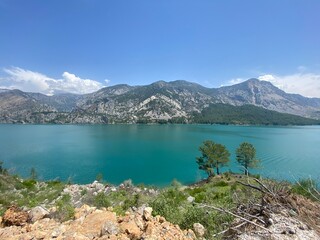 Scenic view of Green Canyon in Turkey with turquoise lake and mountain range in background. Summer travel destination with clear sky and natural landscape.