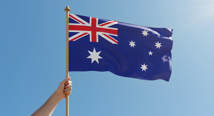 Hand Holding Waving Australian Flag Against Clear Blue Sky