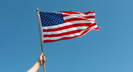 Waving American Flag Held by Hand Against Clear Blue Sky