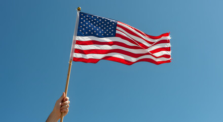 Hand Holding American Flag Waving Against Clear Blue Sky, Symbolizing Patriotism and Freedom
