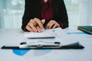 A businesswoman analyzes financial documents with charts and graphs at a desk, highlighting data trends with a pen in a bright, professional office setting.	