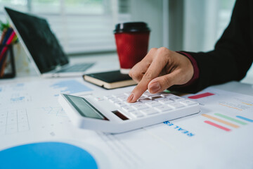 A businesswoman analyzes financial documents with charts and graphs at a desk, highlighting data trends with a pen in a bright, professional office setting.	