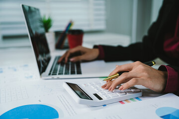 Fototapeta premium A businesswoman analyzes financial documents with charts and graphs at a desk, highlighting data trends with a pen in a bright, professional office setting. 