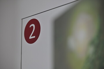 A red number 2 on a glass door with blurred white wall and green area.