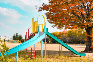 Colorful playground equipment in an autumn park with a vibrant tree.