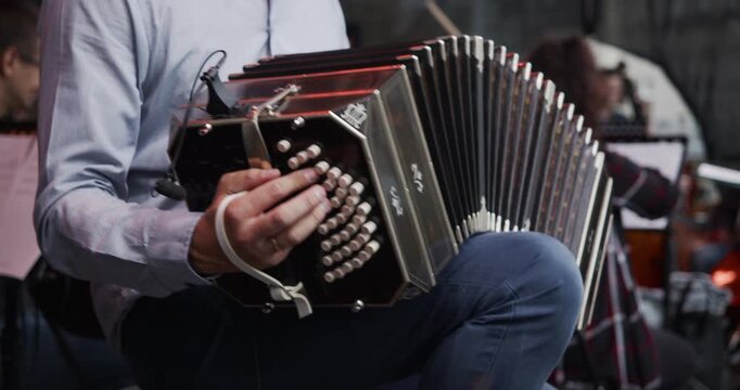 A musician playing a traditional bandoneon in an orchestra or tango ensemble. The player's hands work the buttons and stretch the bellows of the classic instrument. 