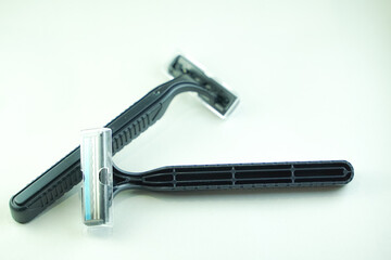 Two black disposable razors are stacked on a white surface, one slightly overlapping the other.