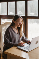 Woman content creator working with laptop. Female in cozy sweater consulting on-line. Remote work, study, SMM, UGC