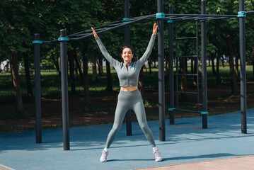 young slim caucasian woman doing jumping jack exercises outdoors in summer, street sports ground,...