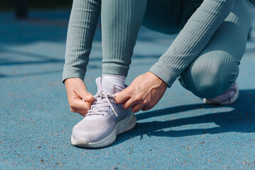 young sportive woman lacing up shoes before doing sport exercises outdoors in summer, white and...