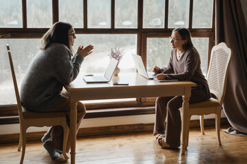 Two young women are collaborating on startup Working with laptops, having discussion. Female business, working remotely, listen attentively Strategic planning, cooperation, and brainstorming concepts