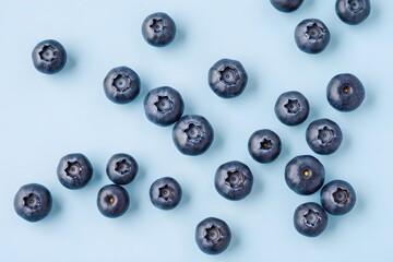Top view of scattered fresh blueberries on pastel blue background, minimalist 