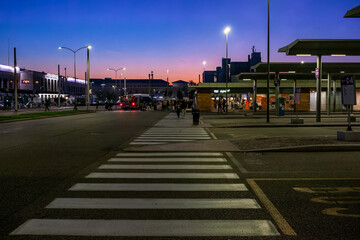 Pedestrian Crosswalk in the Foreground of a Bustling Transit Hub at Dusk