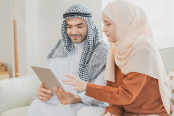 Muslim couple sitting on a sofa at home using a tablet together, smiling and bonding through muslim couple technology moments, showing modern connection and muslim couple technology lifestyle